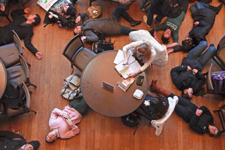 As protesters lie on the floor in a die-in around them, two students sitting at a table in the DUC continue to work.
