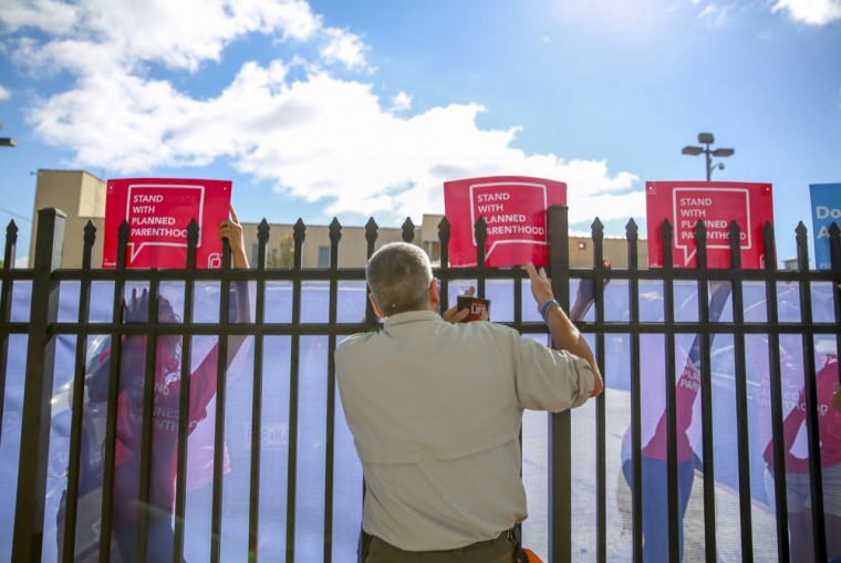 A member of Operation Save America preaches to Planned Parenthood supporters through a fence lined with blue plastic to protect the identities of supporters. Organizers from Planned Parenthood instructed supporters to not engage with protesters.