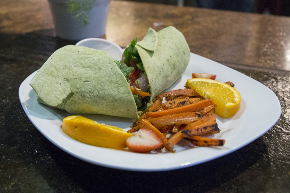 A jerk chicken wrap is served with fruit and vegetables at It’s A Wrap.