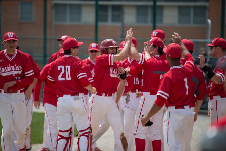 Senior Auggie Mense is congratulated by his teammates outside the dugout after scoring the Bears’ opening run in the first game against Case Western Reserve University April 21.