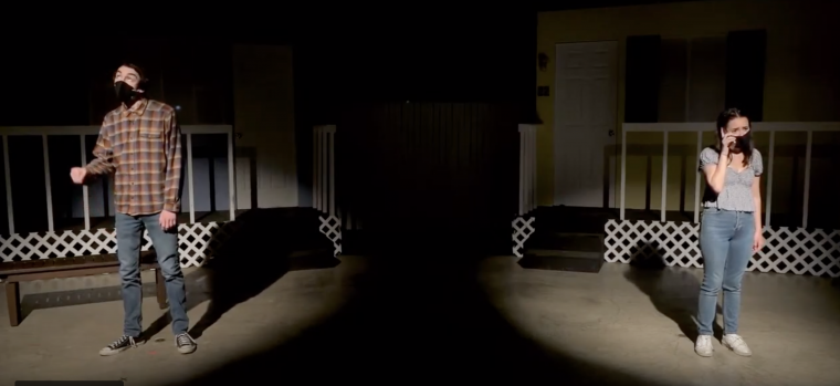 Two spotlights illuminate the left and right thirds of the photo. A man stands in the left spotlight and a woman in the right.