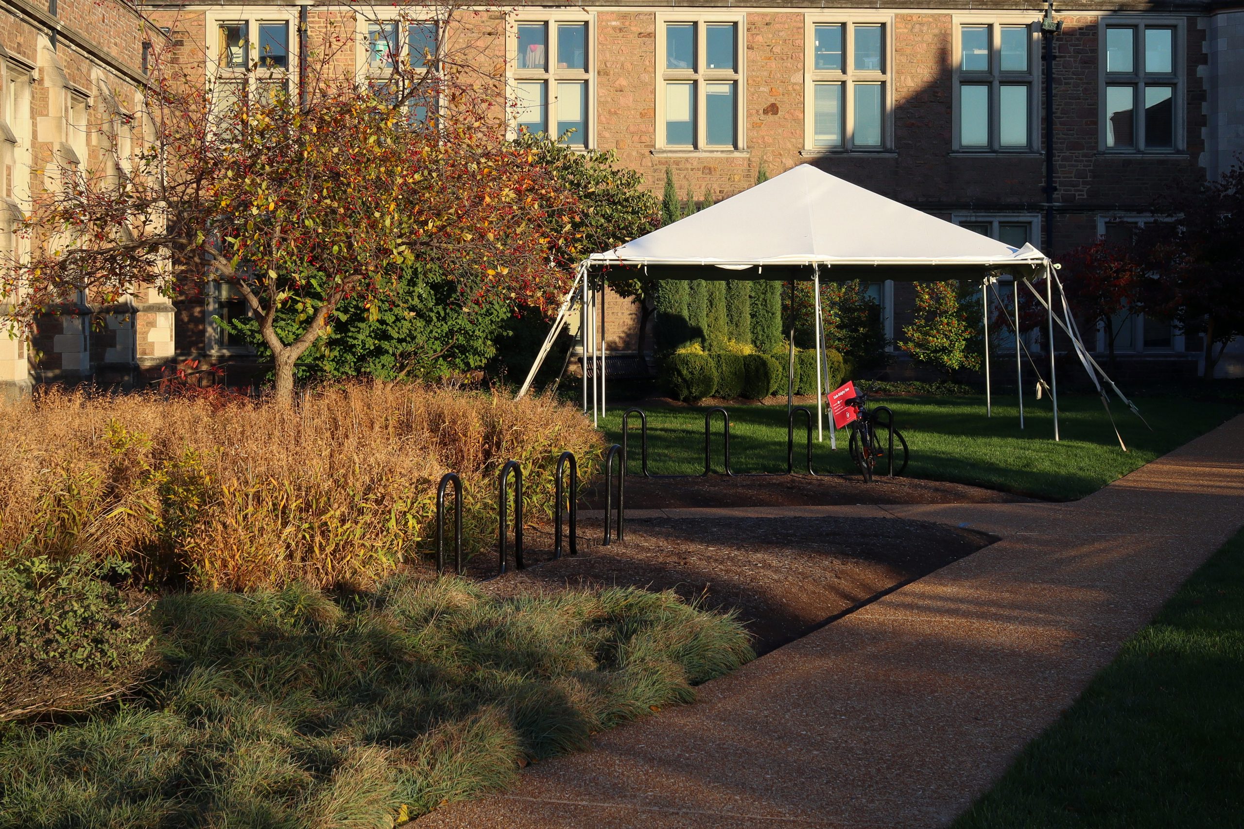 A white tent stands on a patch of green grass in front of two multistory brick buildings