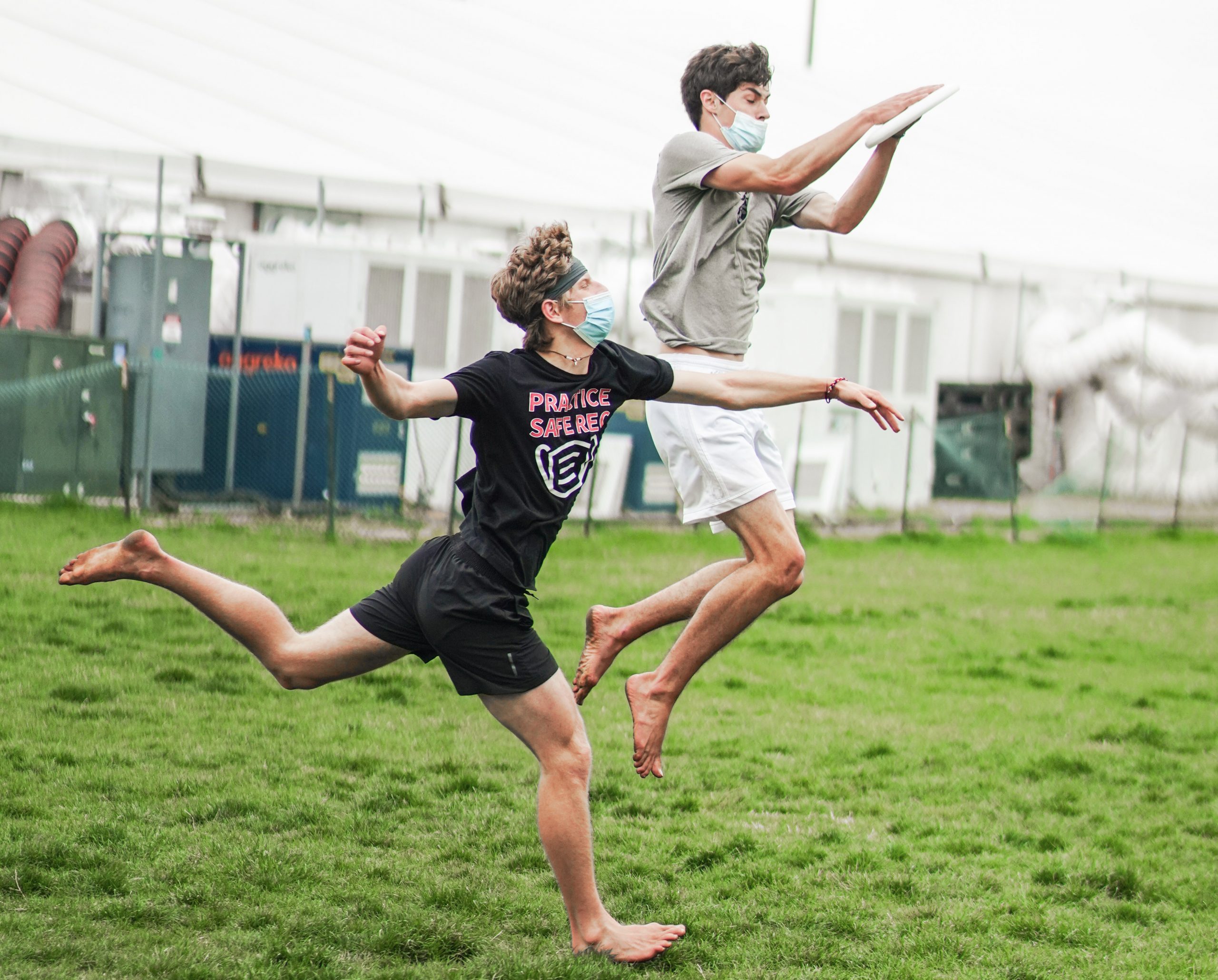 One student jumps in the air to catch a frisbee as another chases them.
