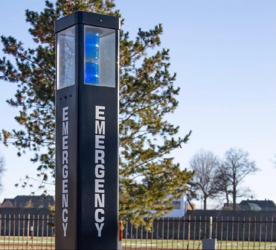 A blue light on campus in front of a green tree and blue sky