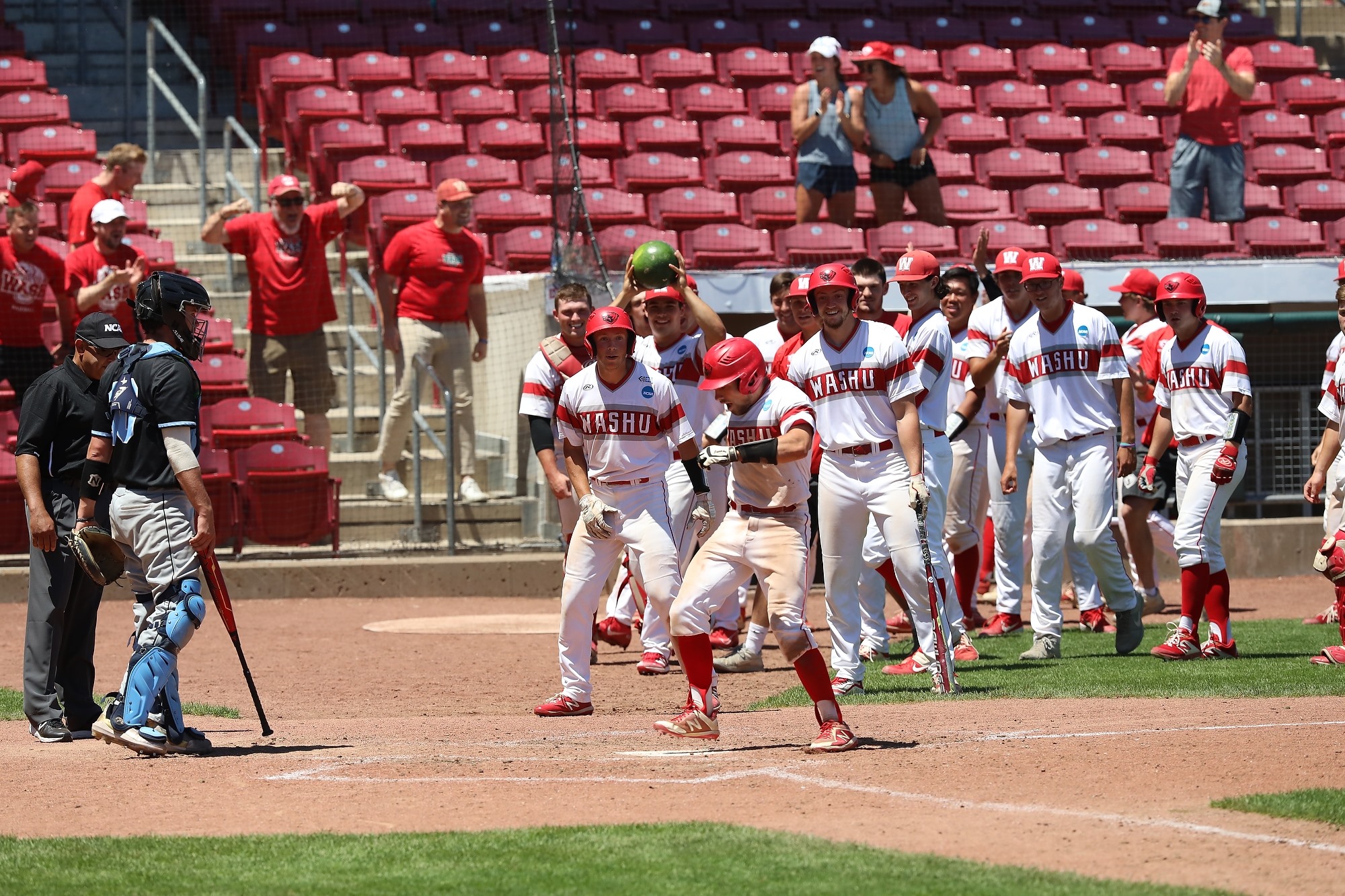 A crowd of baseball players lines up to greet a player with high red socks near home plate with red seats in the background.