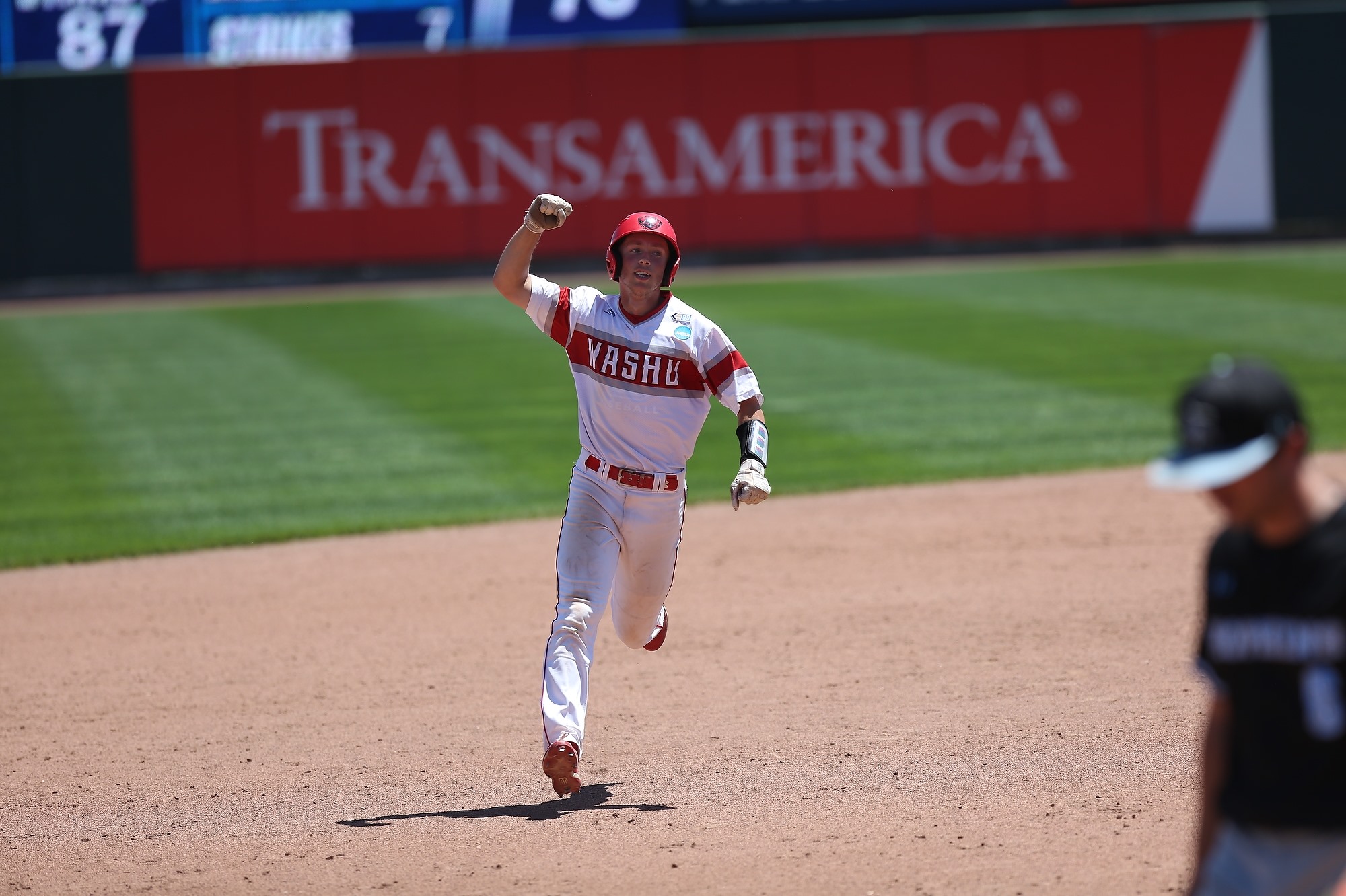 A baseball player in a white uniform pumps his fist as he rounds the bases. A sign in the outfield behind him says "TransAmerica."