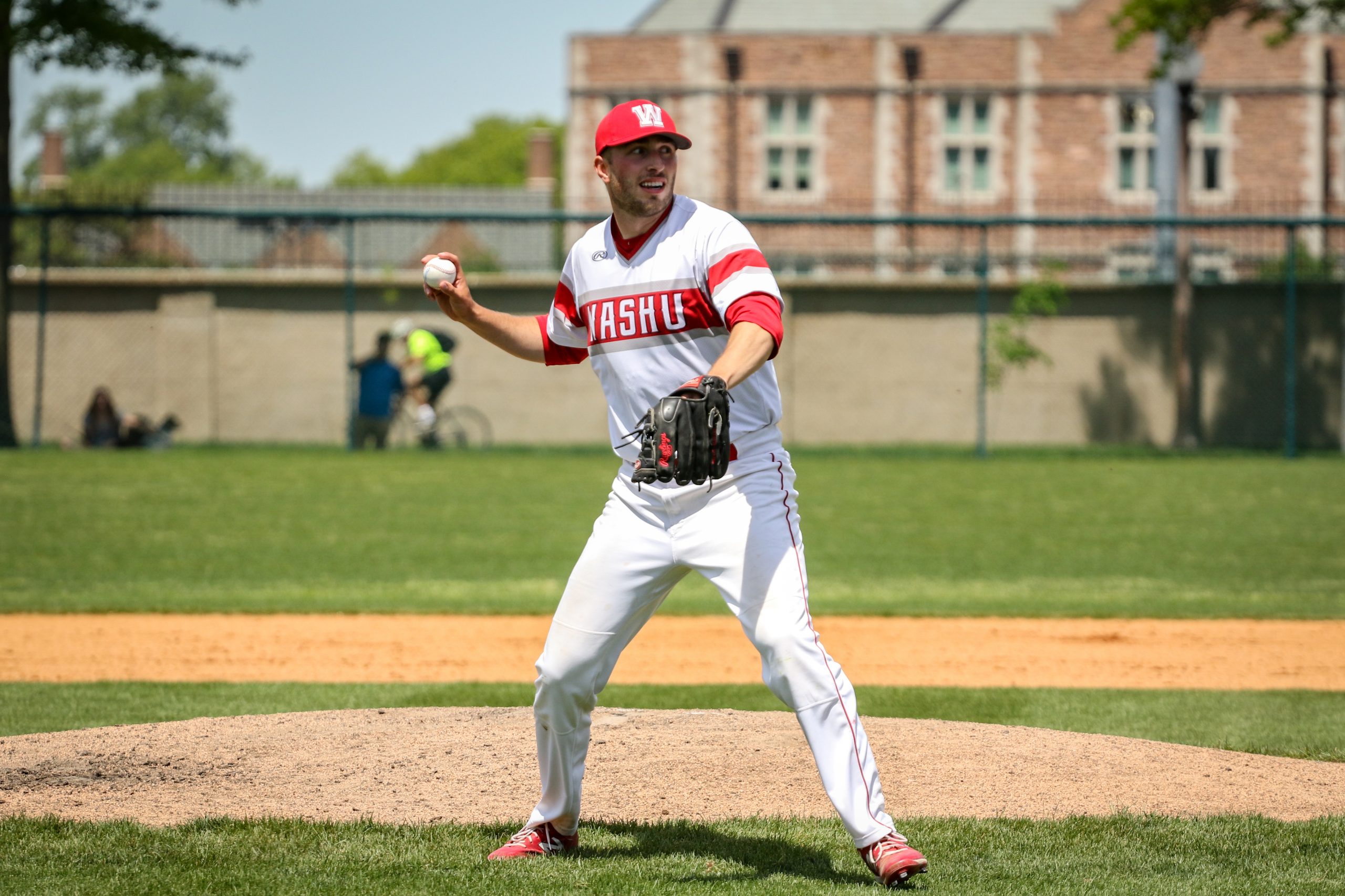 A player in a white uniform with red trim brings his right arm back to toss a ball on the infield.