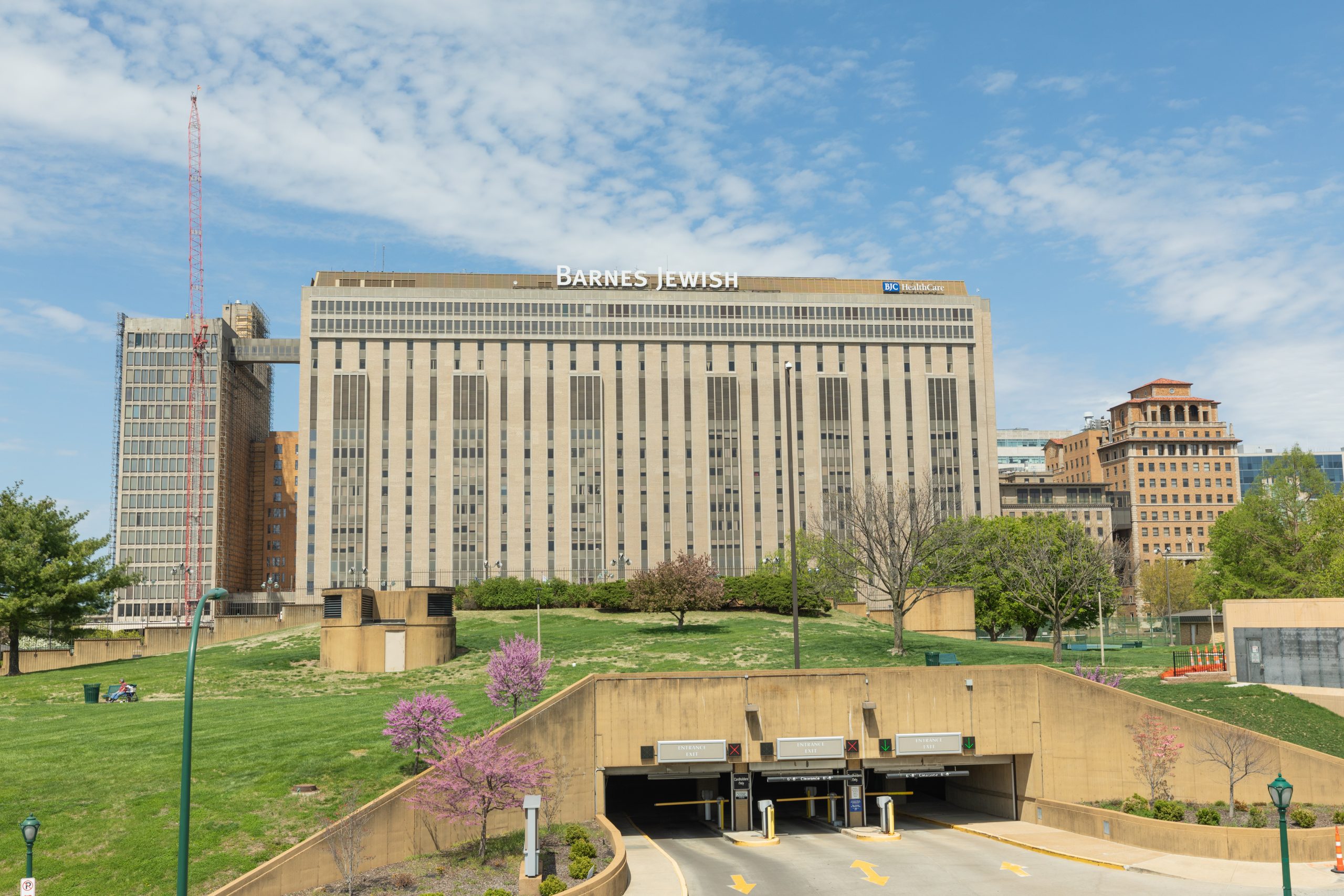 A large building complex stands behind a grassy park area, with a blue and slightly cloudy sky in the background.