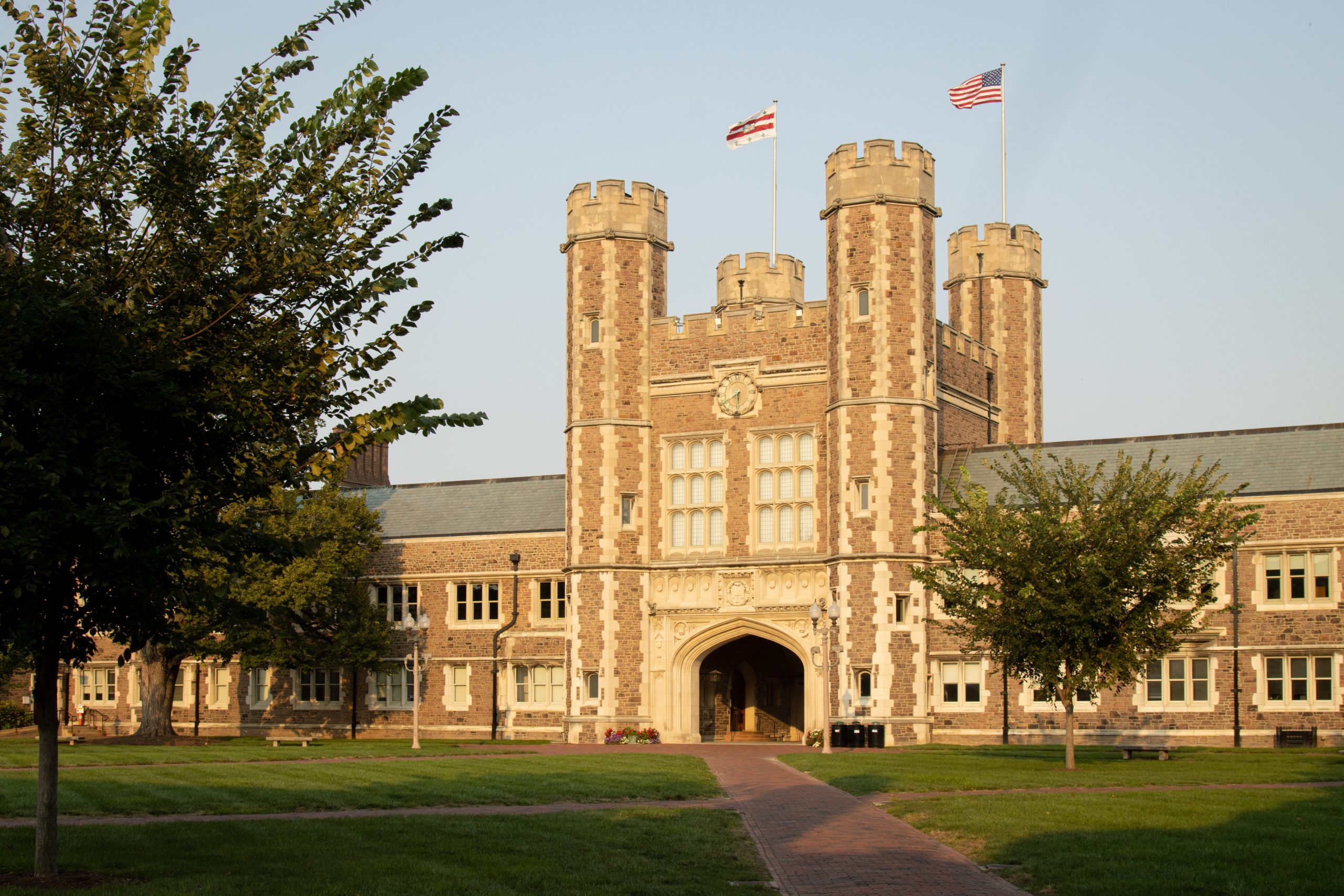 A white and red brick building with four small towers stands over a green lawn crossed by brick paths