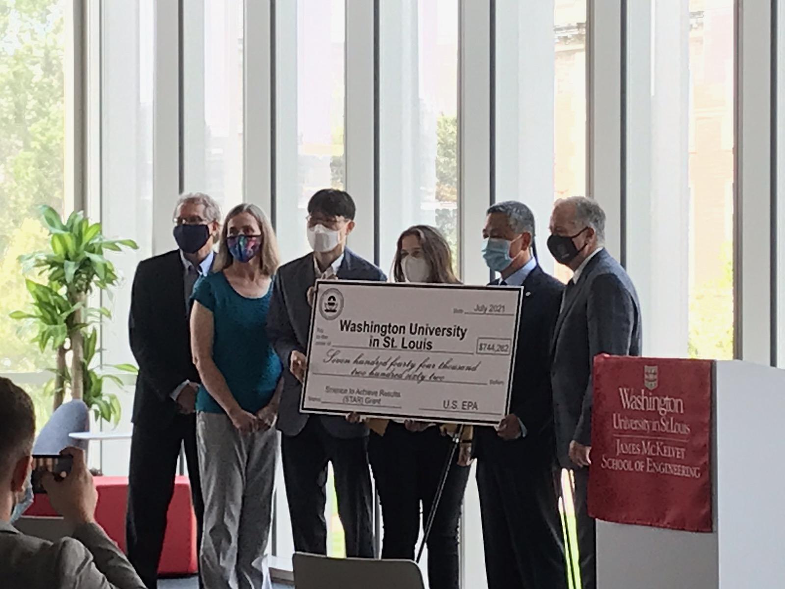 Several individuals stand in a row holding up an enlarged check made out to the University.