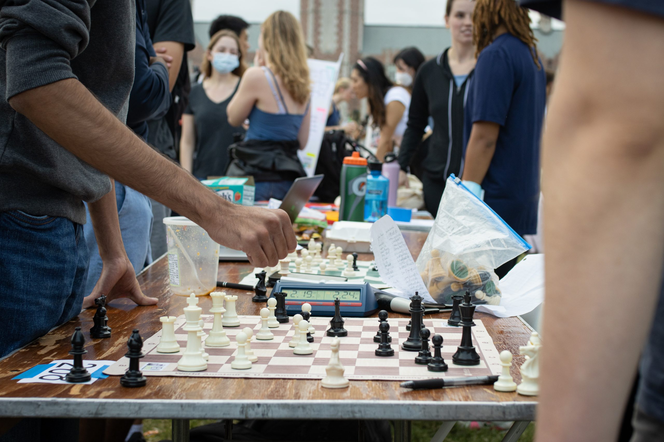 A chess board sits on a table surrounded by students.