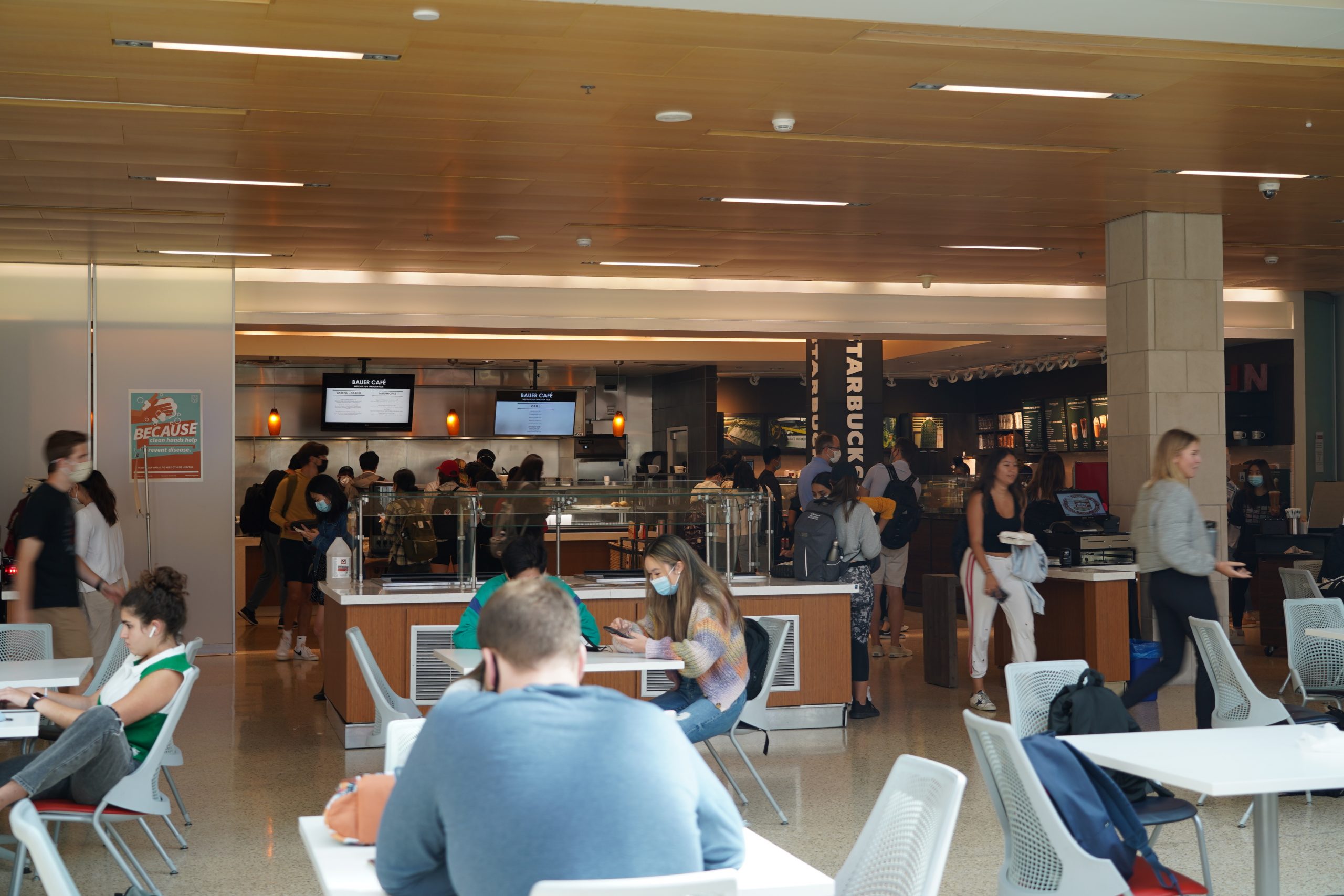 Several people sit at white tables and walk around inside a cafe.