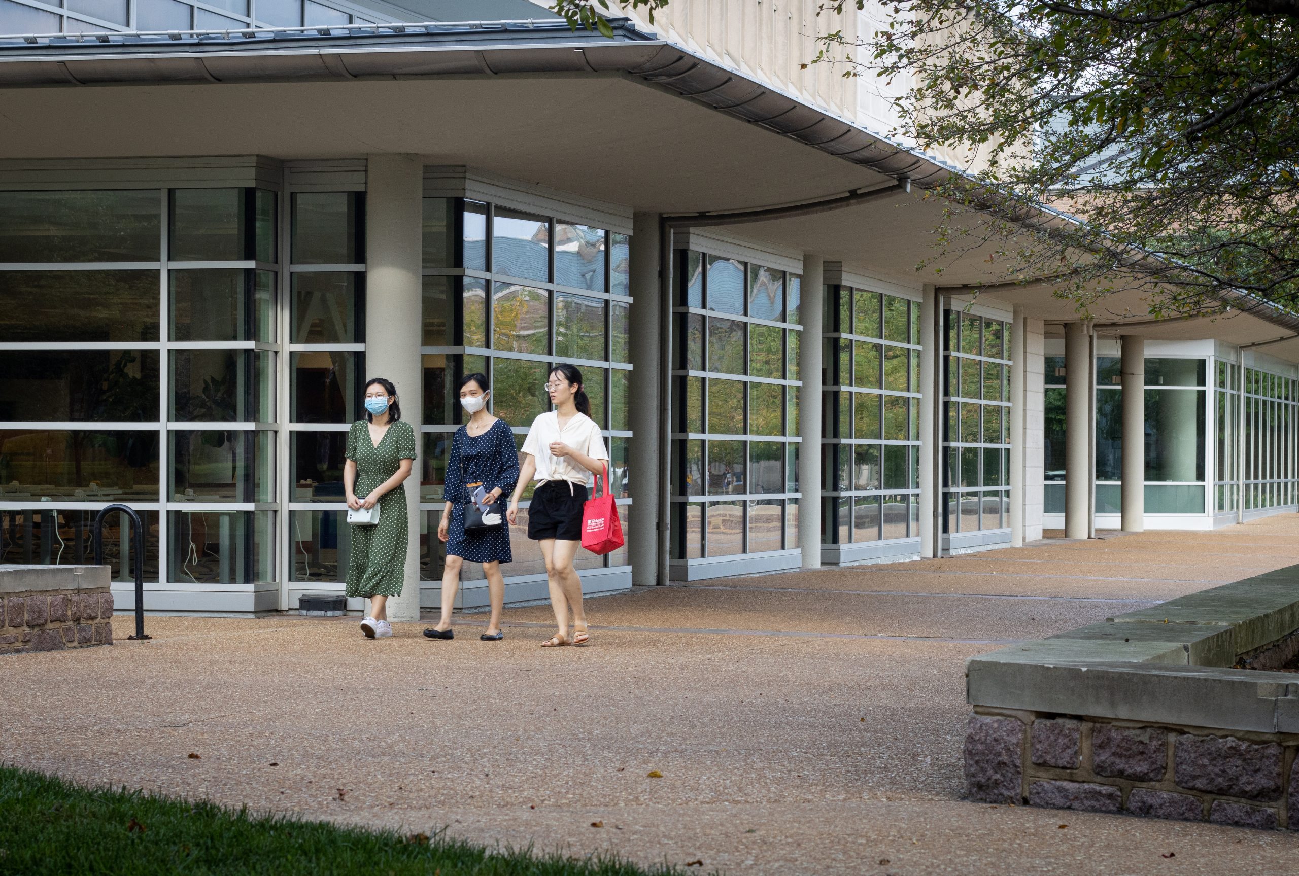 Three people walk next to a building with floor-to-ceiling windows.
