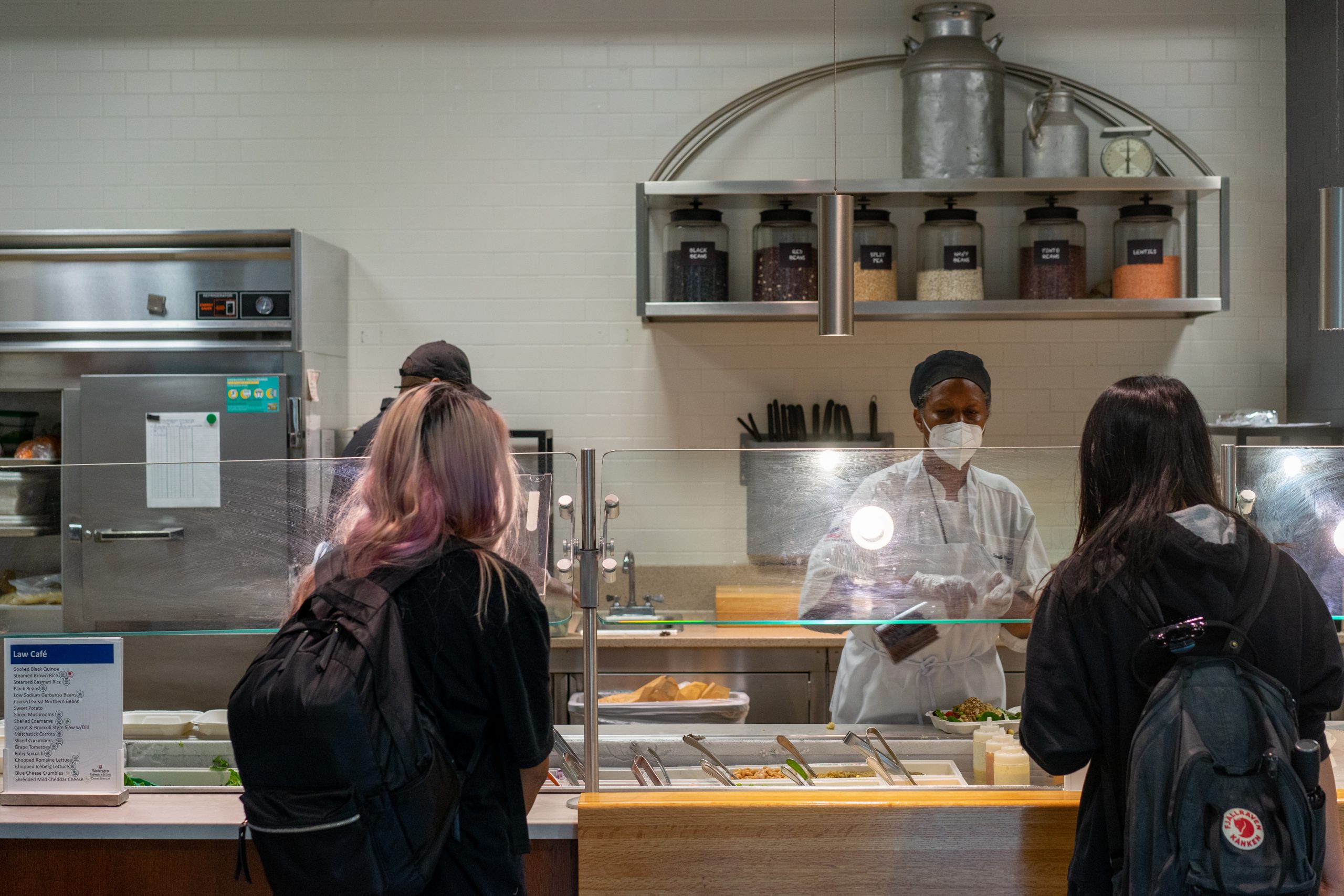 Two students carrying backpacks stand across a counter from a chef.