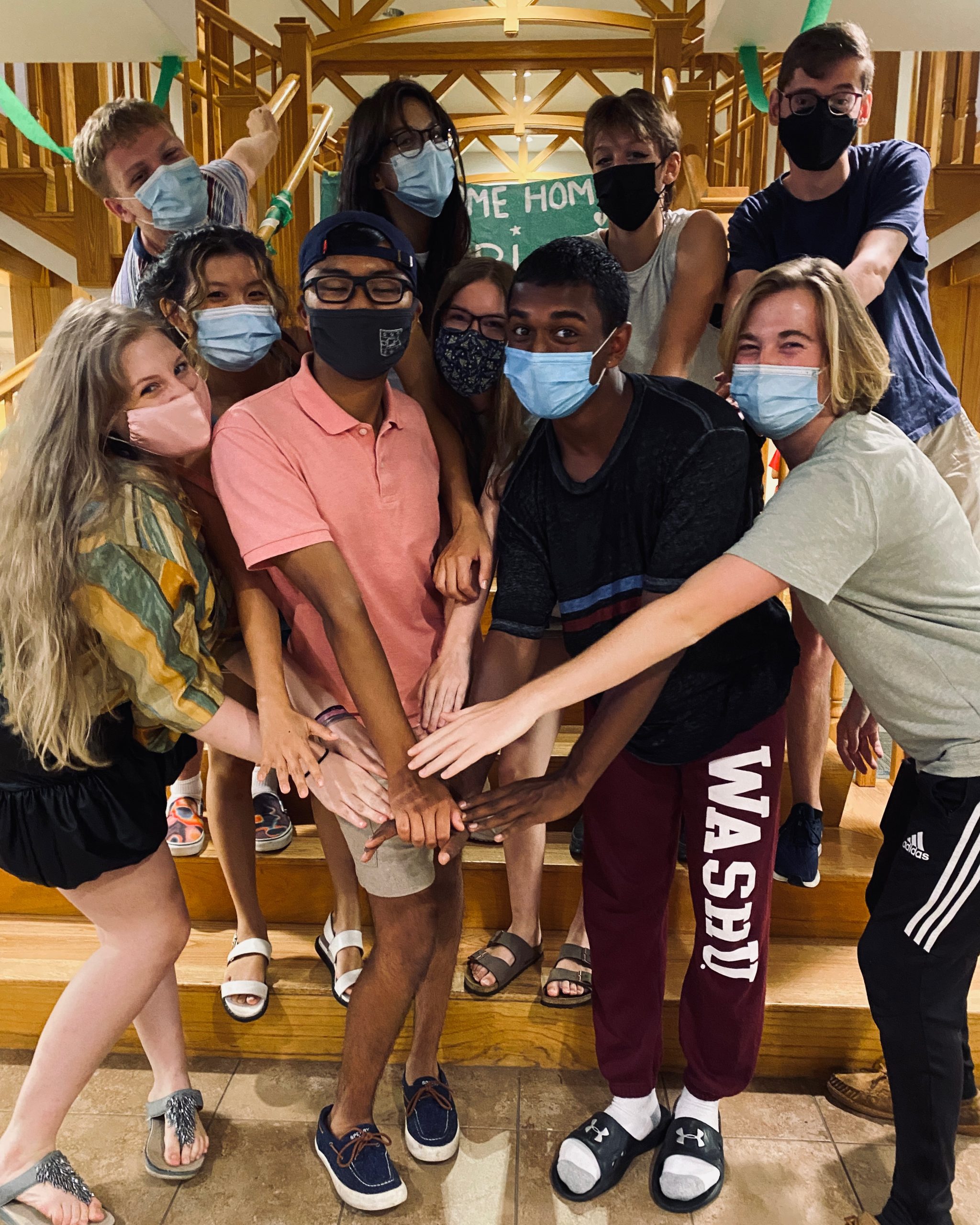 A group of masked students stand together with their hands outstretched.