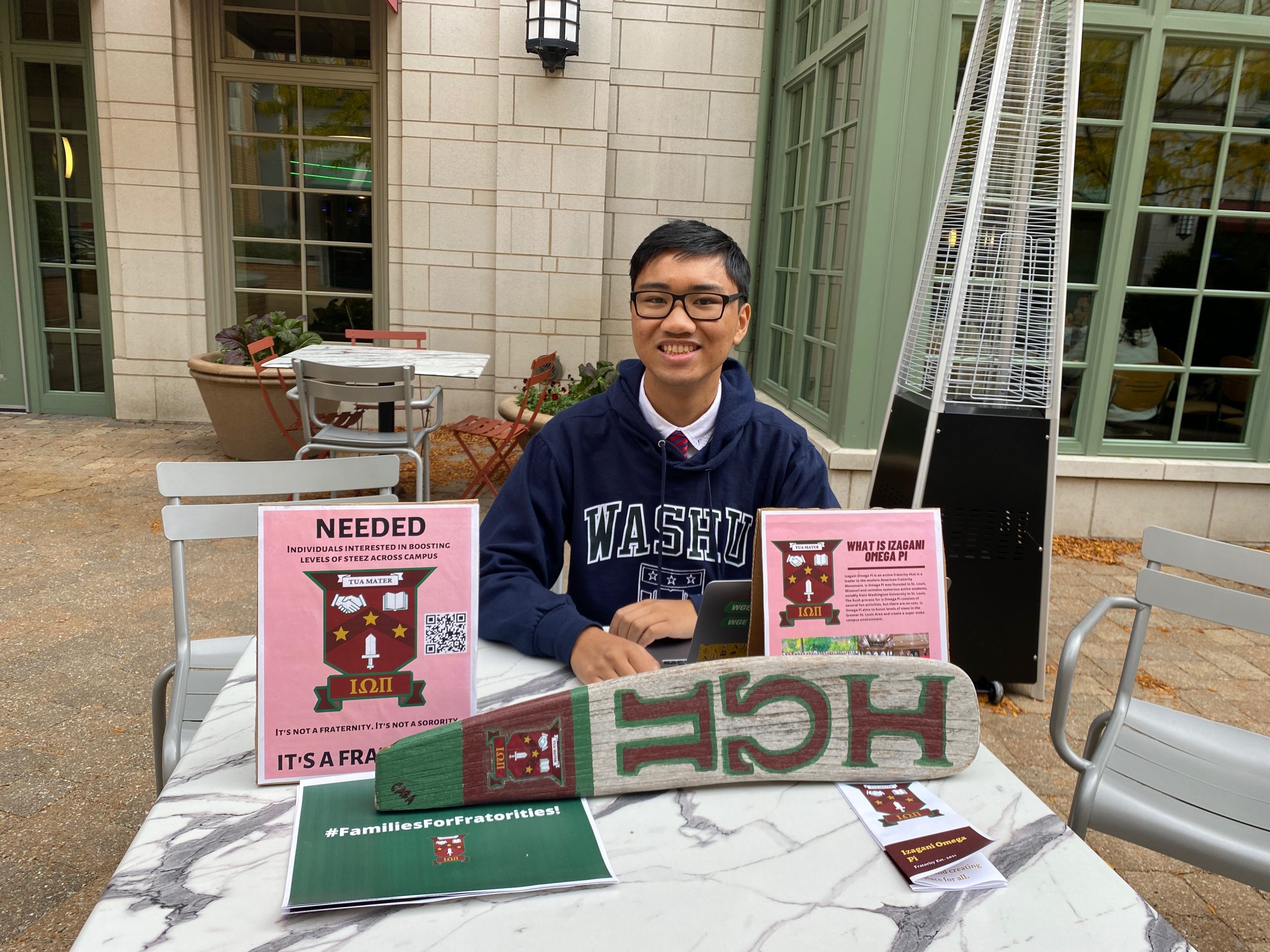 A student sits behind a table with signs reading “Izagani Omega Pi.”