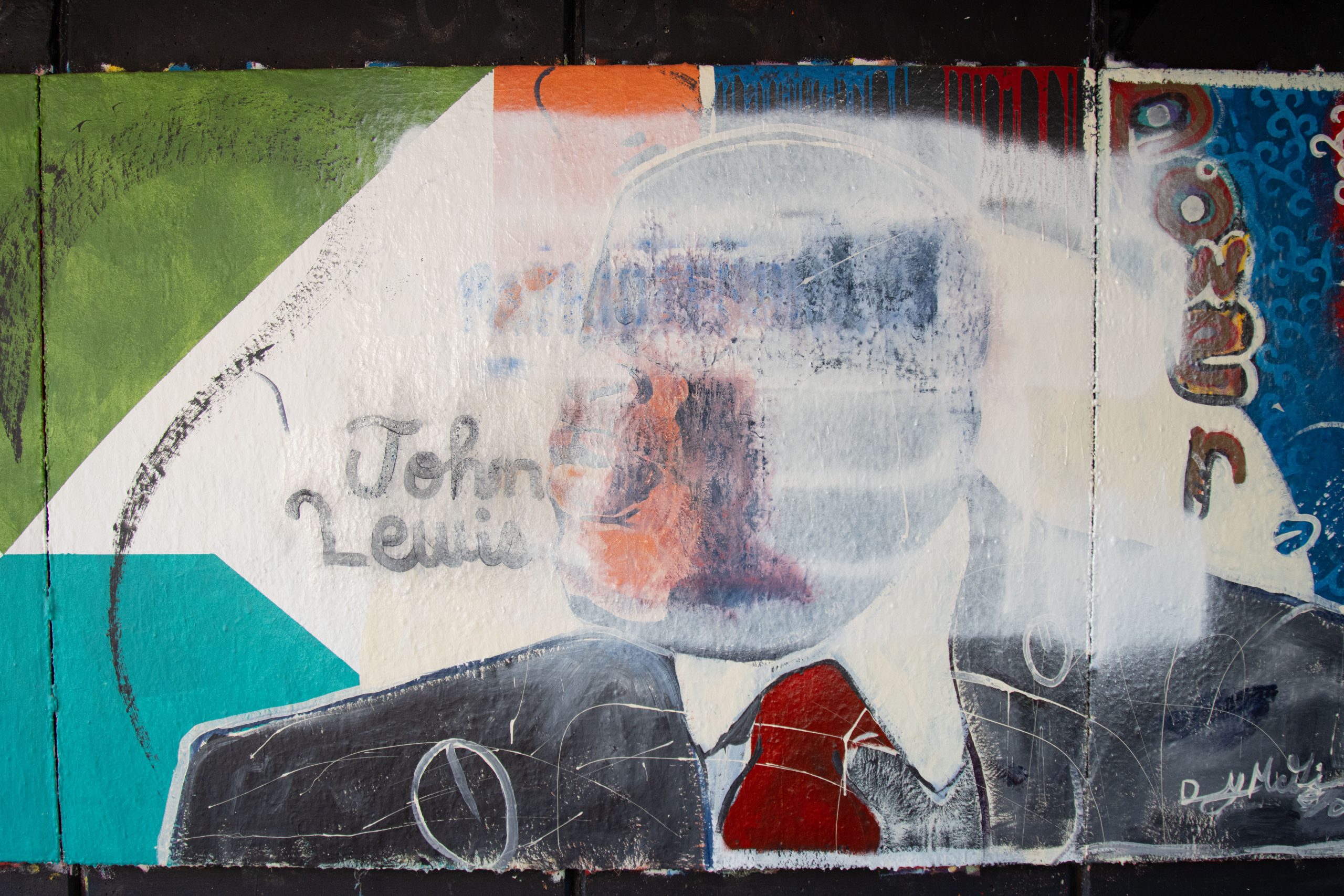 A painted mural of a man in a suit and red tie (and the text John Lewis to the left of his face) is covered by a white paint-like substance.