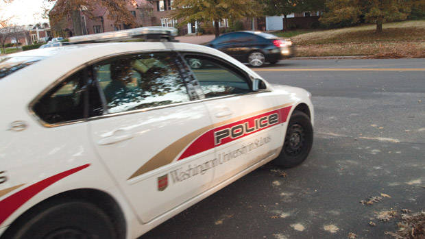 A white police car with a red stripe on its side pulls out into a street.