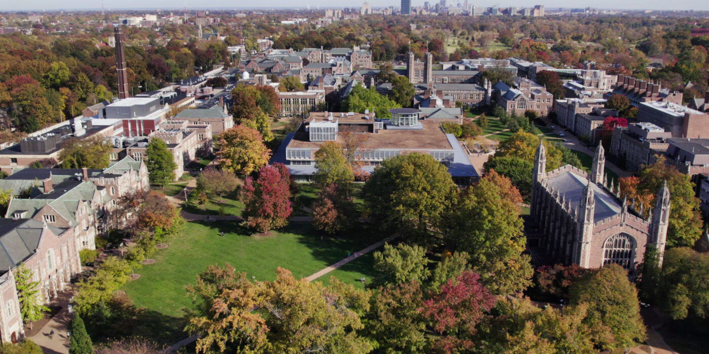 A cluster of brick buildings are seen from an aerial perspective. A green space with trees sits in the center of the buildings.