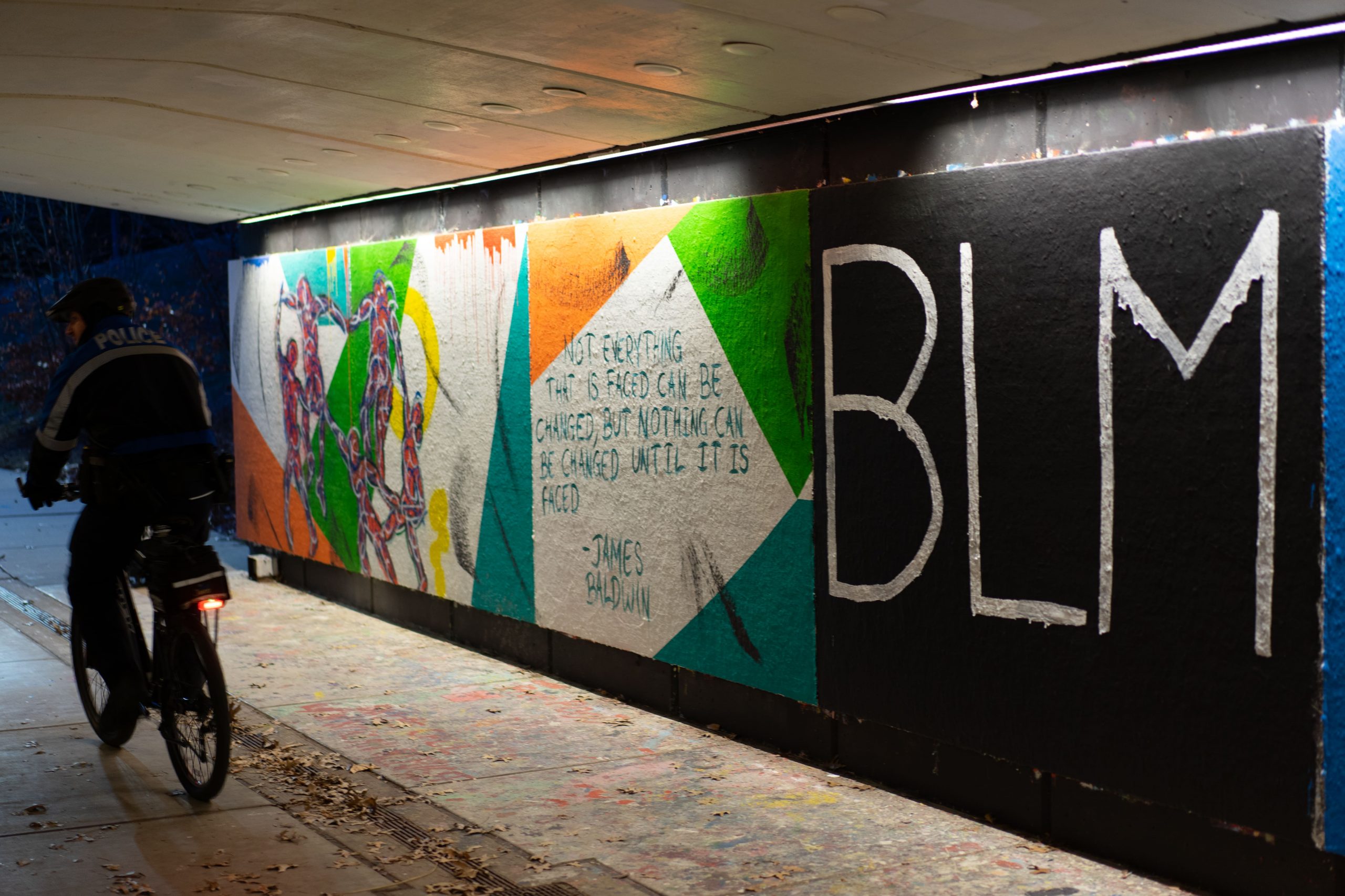A figure on a bike rides past a wall will bright colors on one section and "BLM" written on another