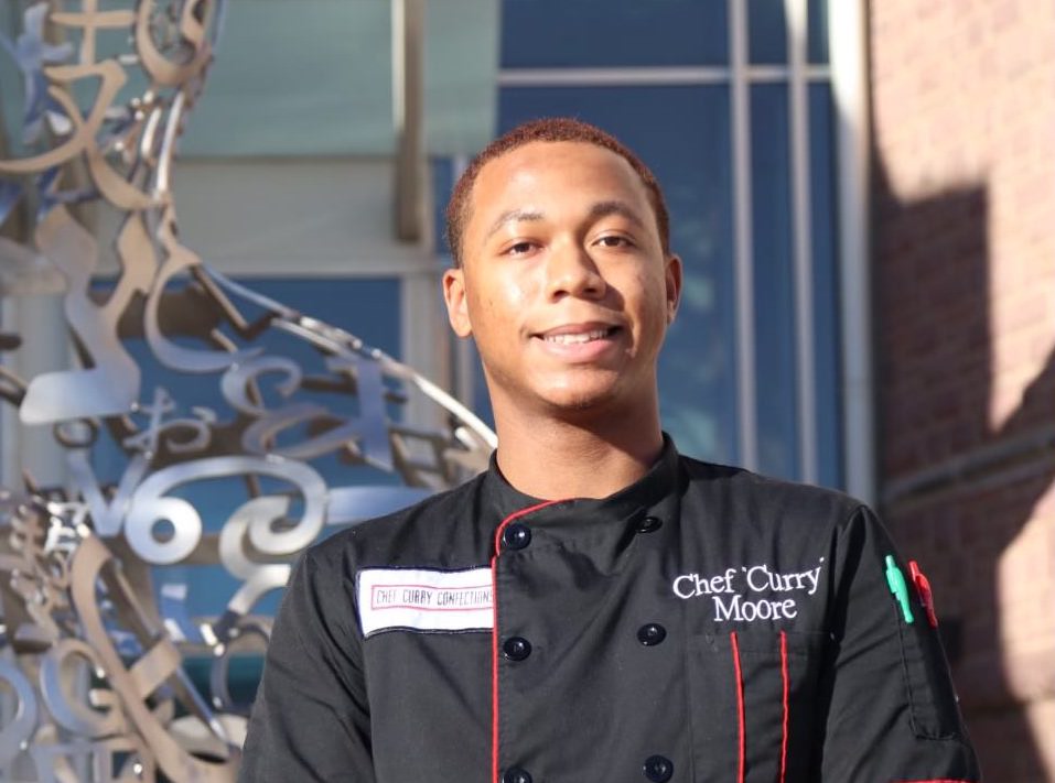 A student wears a black jacket with a label reading "Chef 'Curry' Moore."