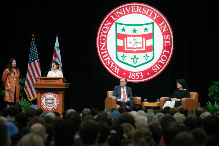 Four people stand on a stage–– Sotomayor, Chancellor Martin, a student with curly black hair, and Dr. G. The WU logo is behind them. 