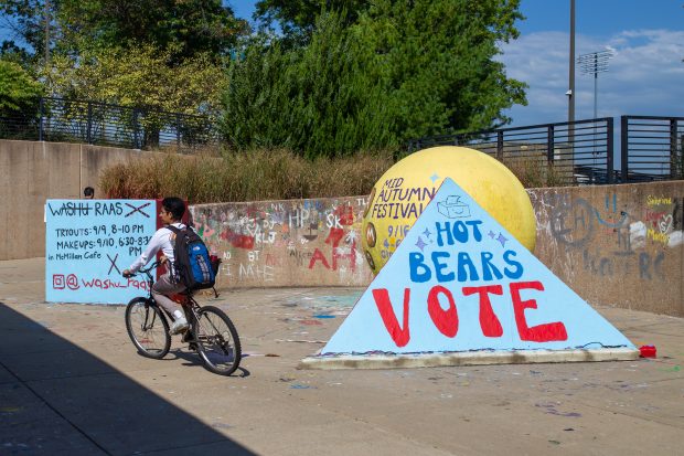 A student bicycles past a pyramid on the underpass that is painted to read, "Hot Bears Vote" in large blue and red letters.